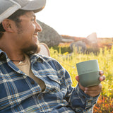 Man holding a green tumbler outdoors with a scenic background