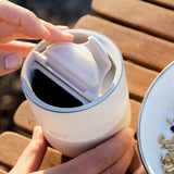 Person holding a white insulated tumbler on a wooden surface.