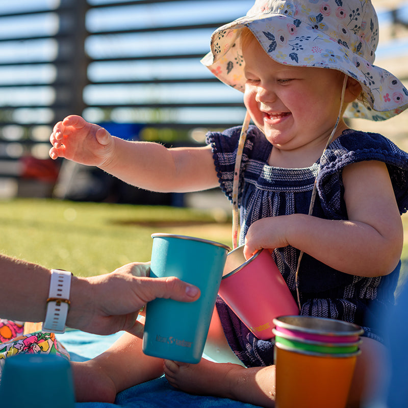 Child in a floral hat holding colorful cups outdoors