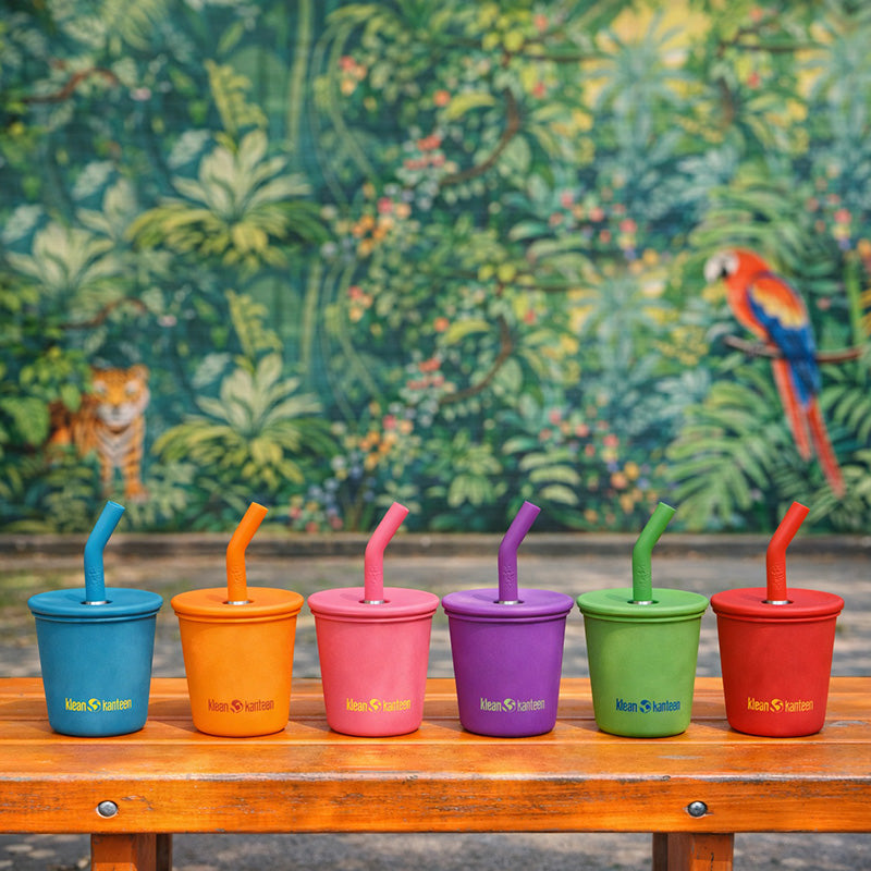 Set of colorful cups with straws on a wooden bench against a jungle background
