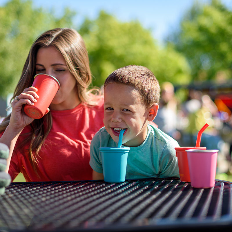 Woman and child at a table with colorful cups and straws outdoors