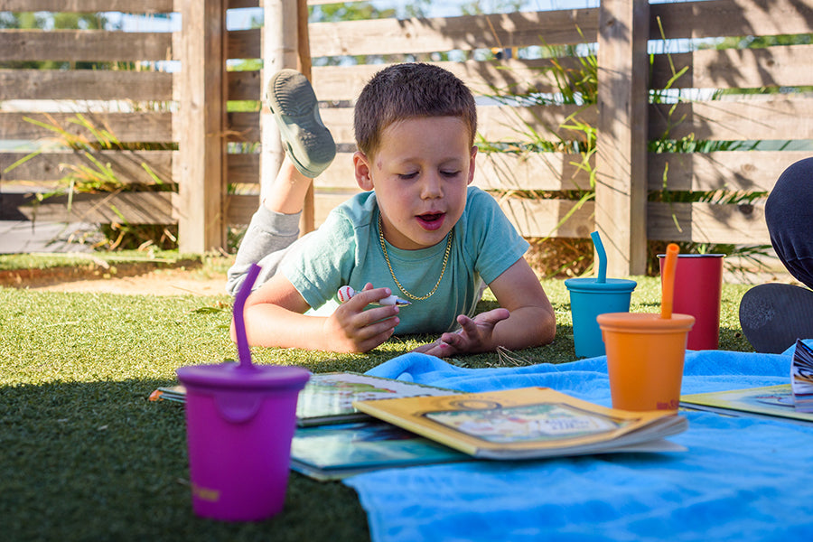 Child playing with toys on a grassy area with colorful cups and books.