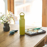Yellow water bottle on a wooden table with flowers and glasses in the background