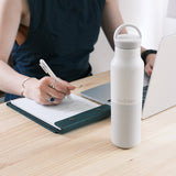 Person taking notes with a pen and notebook on a desk next to a white water bottle.