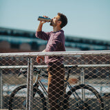Man drinking from a bottle while standing next to a bicycle behind