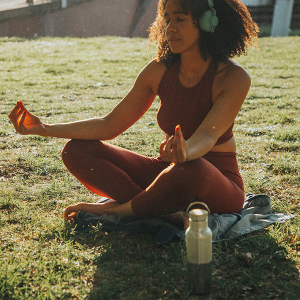 Woman sitting on grass in a yoga pose with a water bottle nearby
