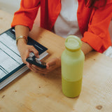 Person using a phone with a yellow water bottle on a wooden table