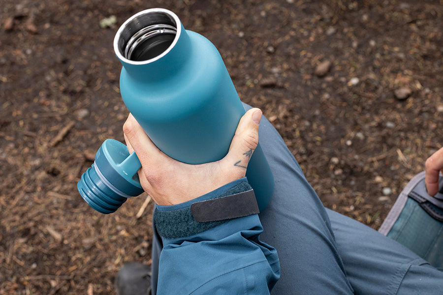 Person holding a blue insulated water bottle with cap off