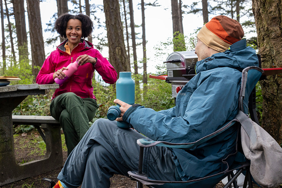 Two people sitting outdoors camping, holding water bottles.