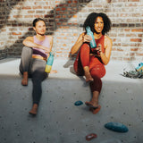 Two women sitting on a ledge with rock climbing and water bottles