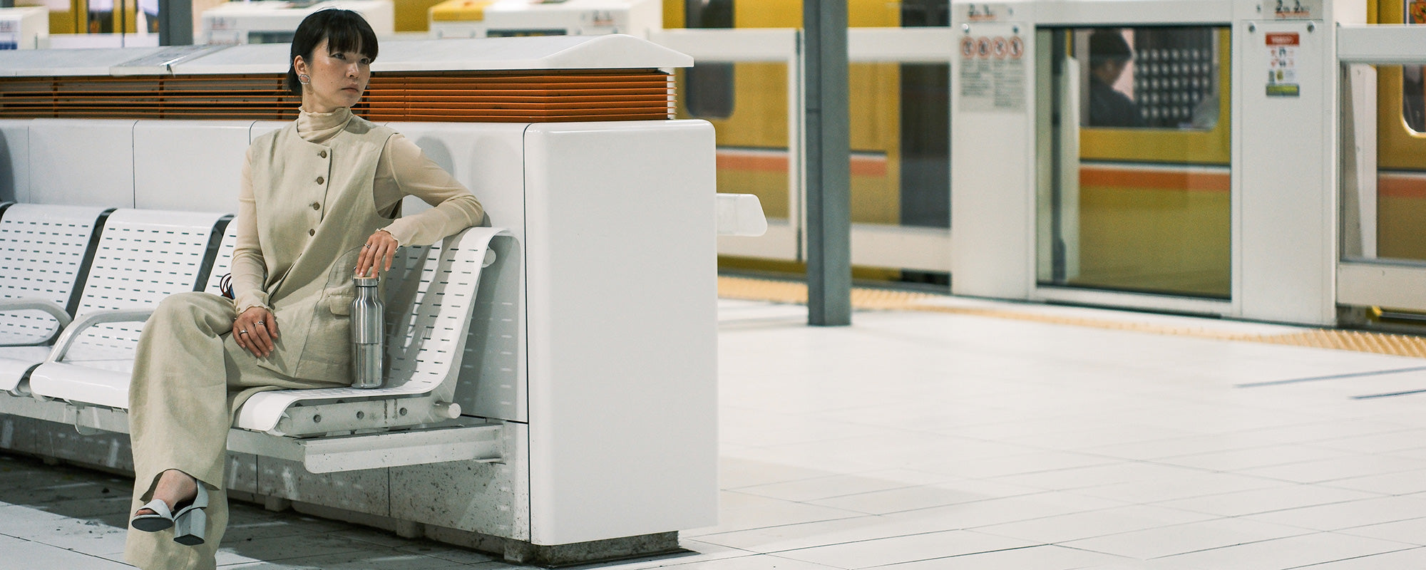 Woman sitting on bench in a train station with Reflect water bottle