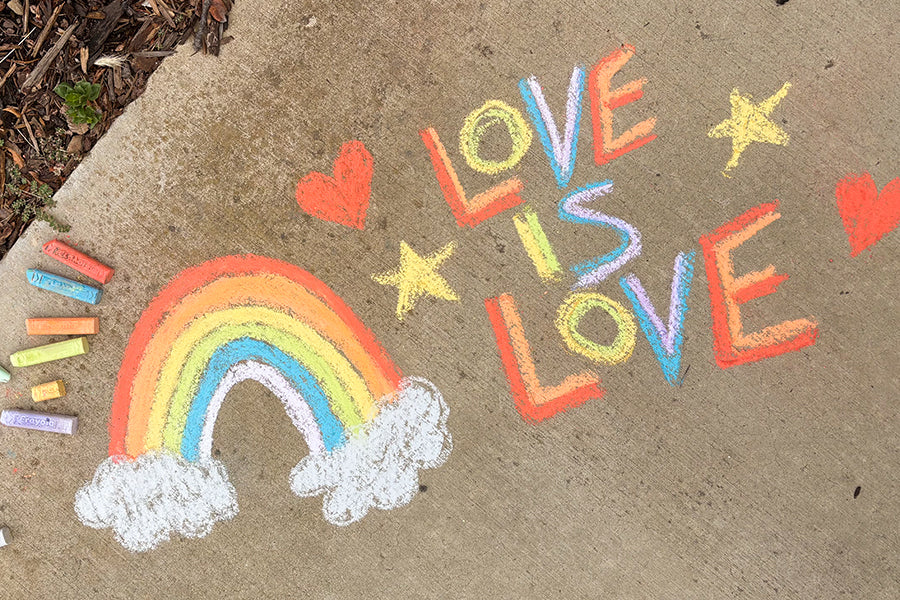 Chalk drawing of a rainbow, hearts, stars, and 'LOVE IS LOVE' on concrete.