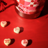 Heart-shaped candies with Valentine's Day messages on a red surface with a Kanteen bottle in the background.