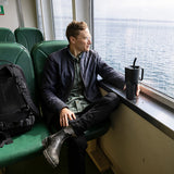 Man sitting on a ferry looking out the window with a tumbler mug in hand