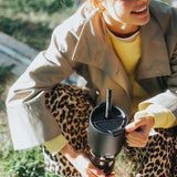 Person holding a black tumbler with a straw lid outdoors