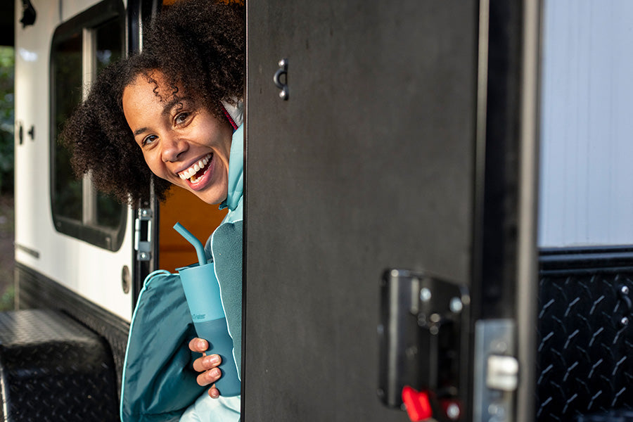 Person peeking out from camper, smiling with tumbler