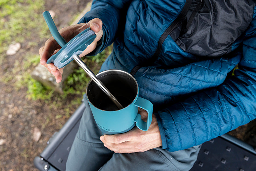 Person in blue jacket holding a blue tumbler with a metal straw