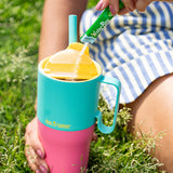 Colorful tumbler with a drink, sitting on grass.