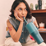 Woman holding a teal tumbler with a straw, sipping drink