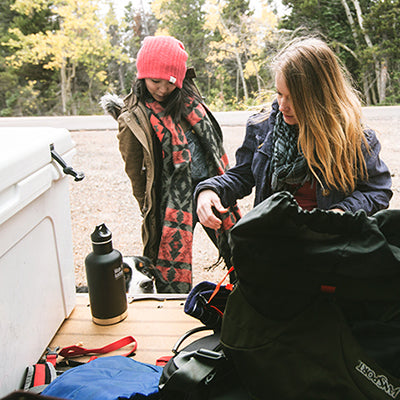 Two people preparing for an outdoor adventure with camping gear in a forest setting.