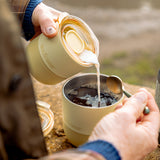 Person pouring cream into a coffee mug outdoors