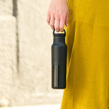 Person holding a black water bottle with a textured yellow garment in the background