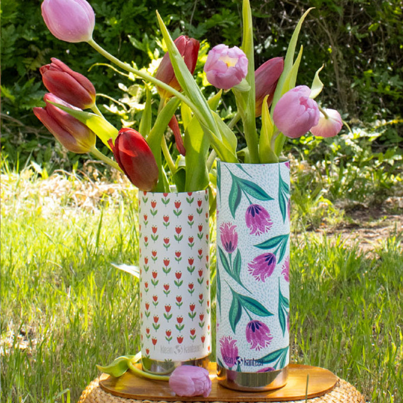 Two floral-patterned water bottles with tulips outdoors on a grassy background