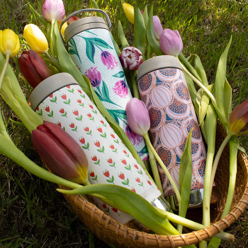 Three graphics water bottles in a basket with tulips on a grassy background