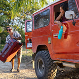 Woman in jeep with teal water bottle, looking out window at person loading luggage