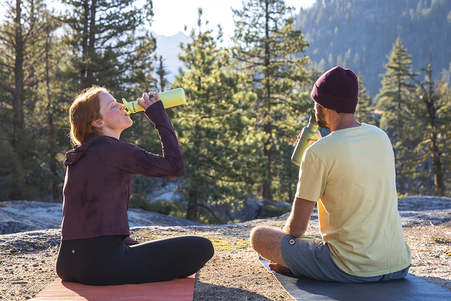 Couple sipping on water bottles after yoga outside
