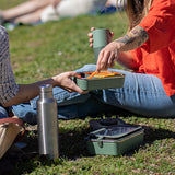 Two people enjoying a picnic on grass with a thermos and food containers.