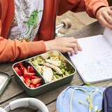 Student eating lunch at a table with a lunchbox containing a salad and strawberries