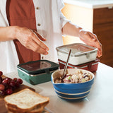 Person preparing a meal with containers and a bowl on a kitchen counter.