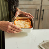 Person holding a steel lunch box with a dish inside on a kitchen counter.