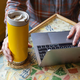 Person using a laptop with a yellow tumbler in coffee shop
