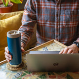 Person holding a blue insulated tumbler with laptop in cafe