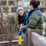 Two people standing outdoors in winter clothing, holding tumblers