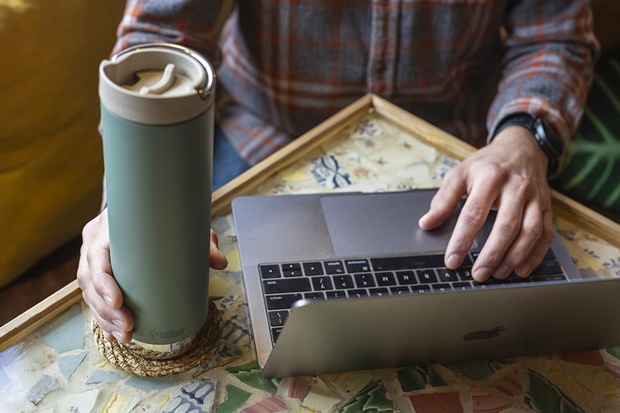 Person using a laptop with a travel mug on a patterned tablecloth