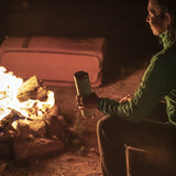 Person sitting by a campfire holding a tumbler