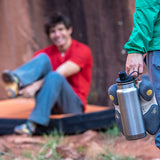 Person holding a water bottle while rock climbing, with person in background
