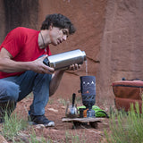 Rock climber outdoors pouring water from a steel bottle into a camping coffee maker.