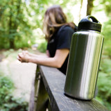 Person sitting outdoors with a stainless steel water bottle on a wooden bench