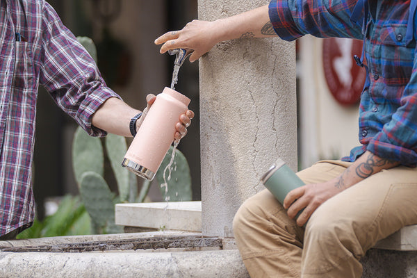 Two people exchanging drink containers near a fountain in a casual setting.