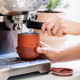 Person using a coffee machine with a red tumbler mug on a light background