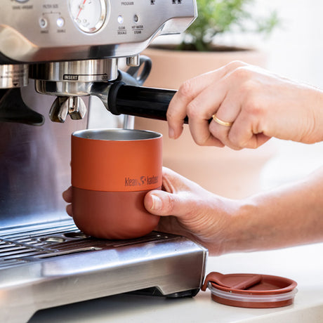 Person using a coffee machine with a red tumbler mug on a light background