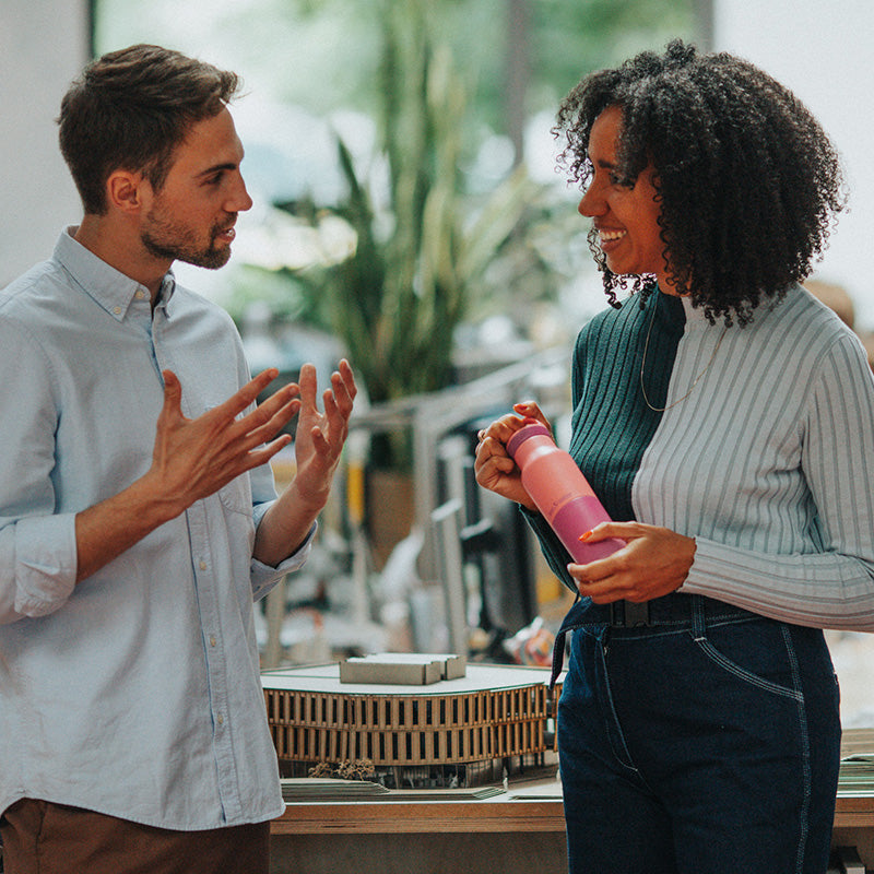 Two people engaged in a conversation with one holding a pink water bottle.