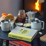 Two coffee mugs on table with food by a fire