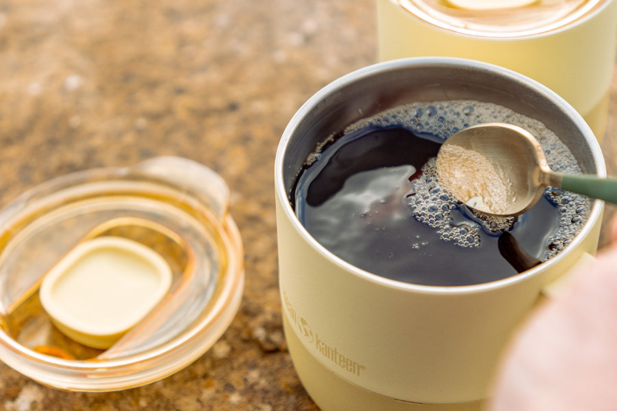 Person stirring a cup of coffee in yellow mug with a spoon on a textured surface