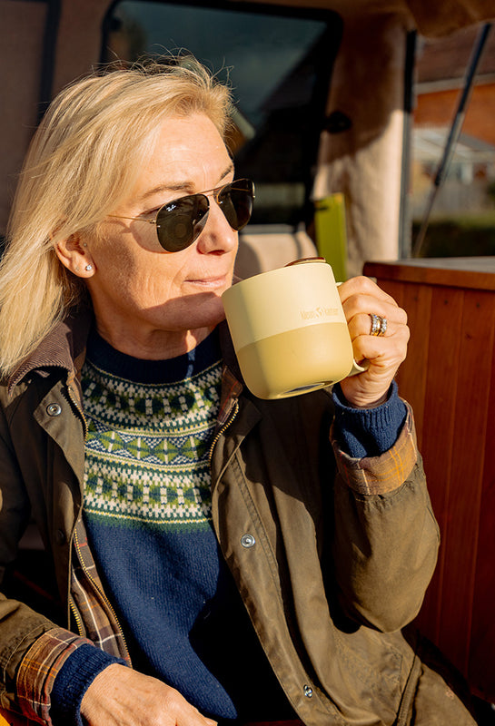 Person wearing sunglasses drinking from yellow coffee mug in camper van