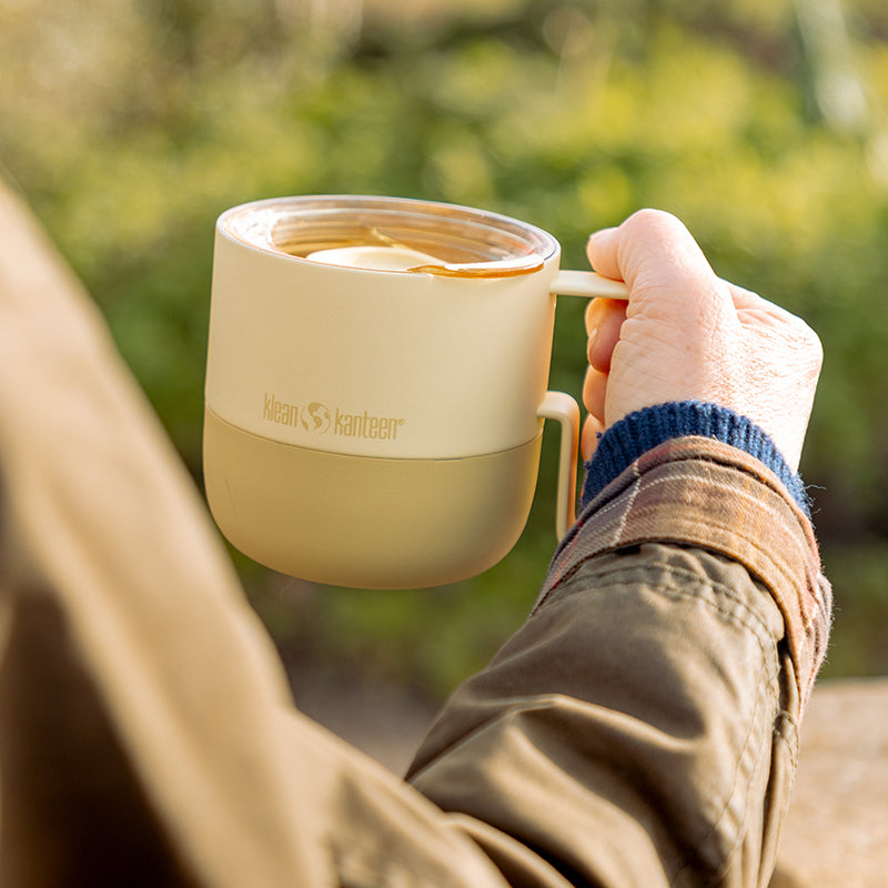 Person holding a yellow Klean Kanteen coffee mug outdoors 